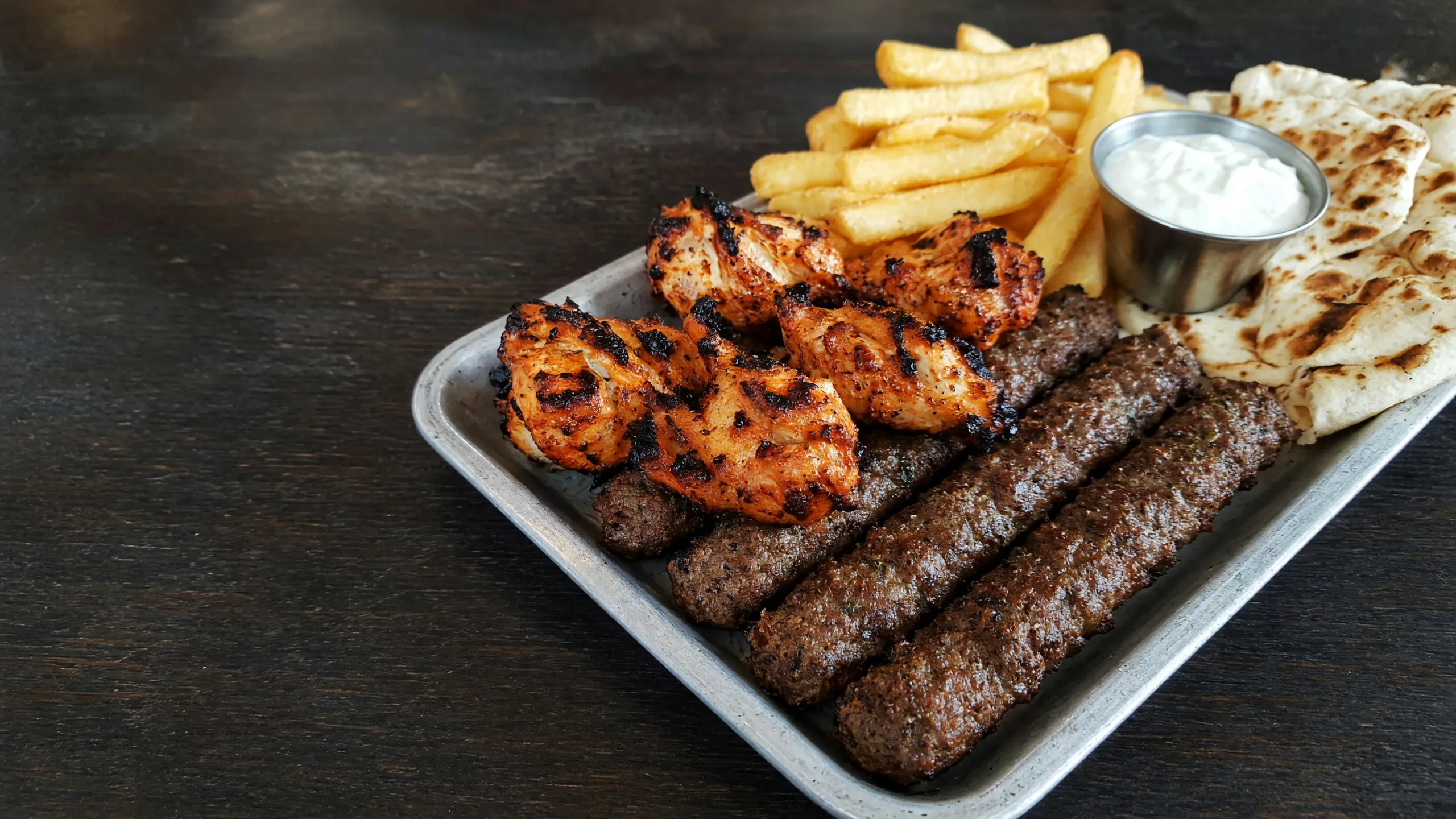 Grilled chicken and beef seekh kebabs on a metal tray with fries and garlic toum